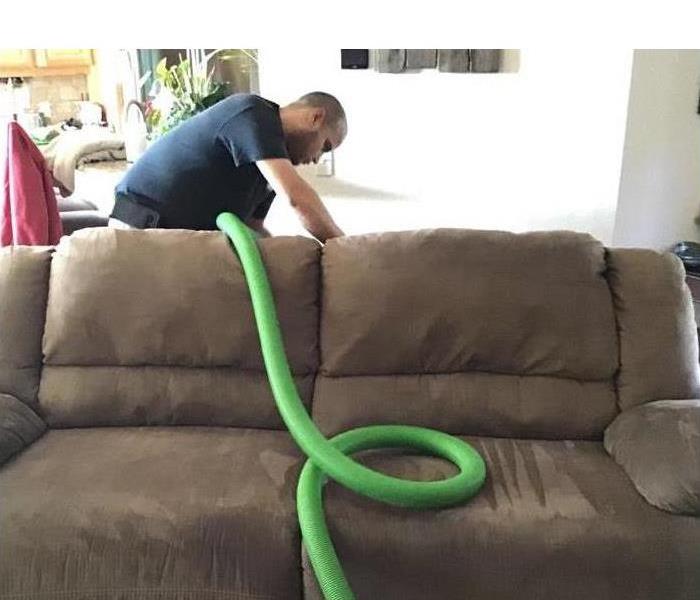 Long green hose draped over couch as technician cleans