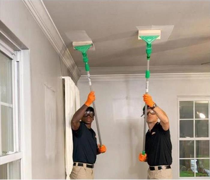 Two Servpro® technicians are cleaning the ceilings of a home