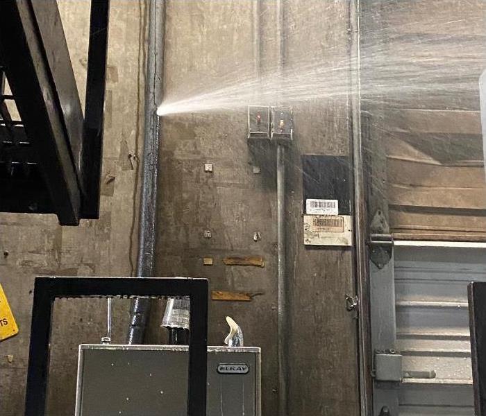 A pipe in a warehouse sprung a leak and water is spraying everywhere