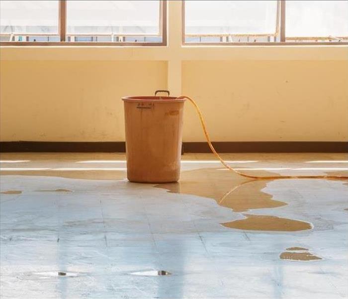 A water bucket sits in the middle of the floor of a commercial building